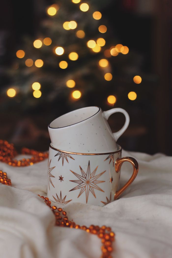 Contact Decorative mugs with Christmas designs set against warm bokeh lights and festive decor.