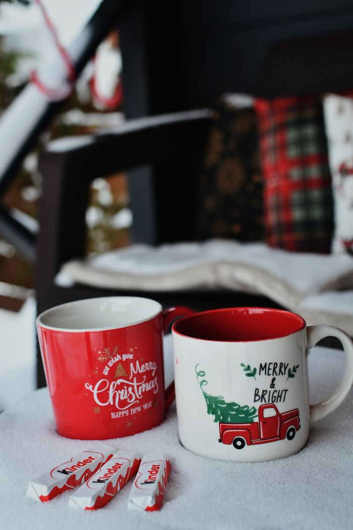 Two Christmas-themed mugs on snowy surface with holiday decorations.