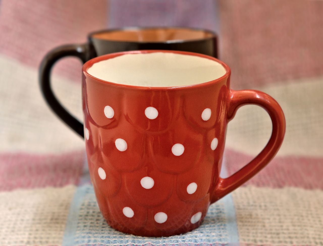 Close-up of a red polka dot mug set on a rustic fabric background, perfect for cozy themes.