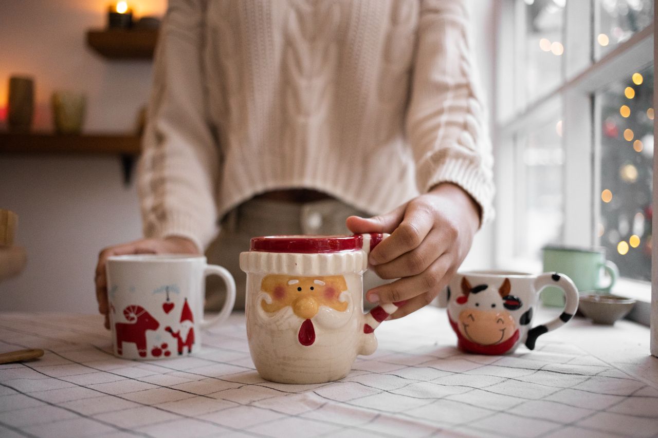Close-up of hands holding decorative Christmas mugs indoors, capturing the warmth of the holiday season.
